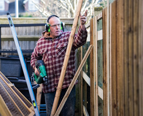 This image shows a fencer installing a fence in a garden